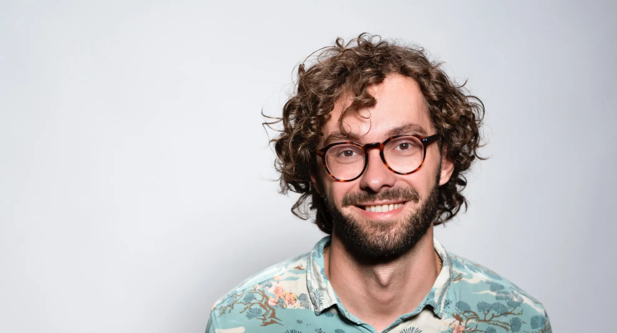 Smiling man with curly hairs, shirt, glasses on brown background