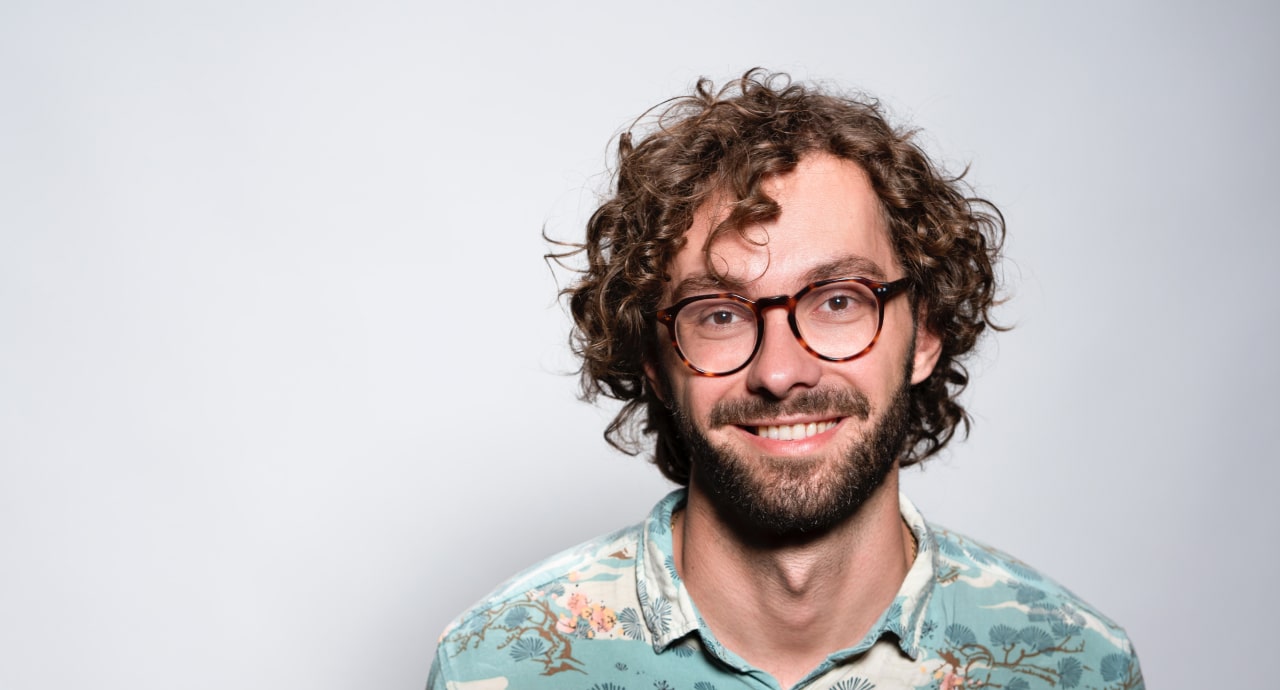 Smiling man with curly hairs, shirt, glasses on gray background