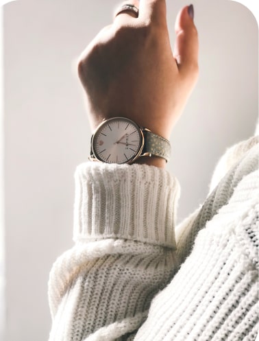 woman dressed in white sweater wears silver watch with white clock face and leather wrist belt