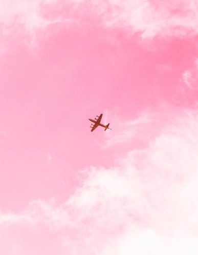a plane in the distance flying under pink sky