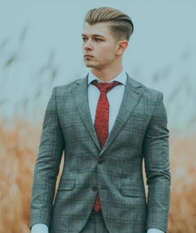 a picture of the groom in a grey suit with red tie standing in the field