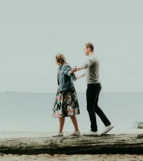 a couple walking near water while holding hands in a lite fog