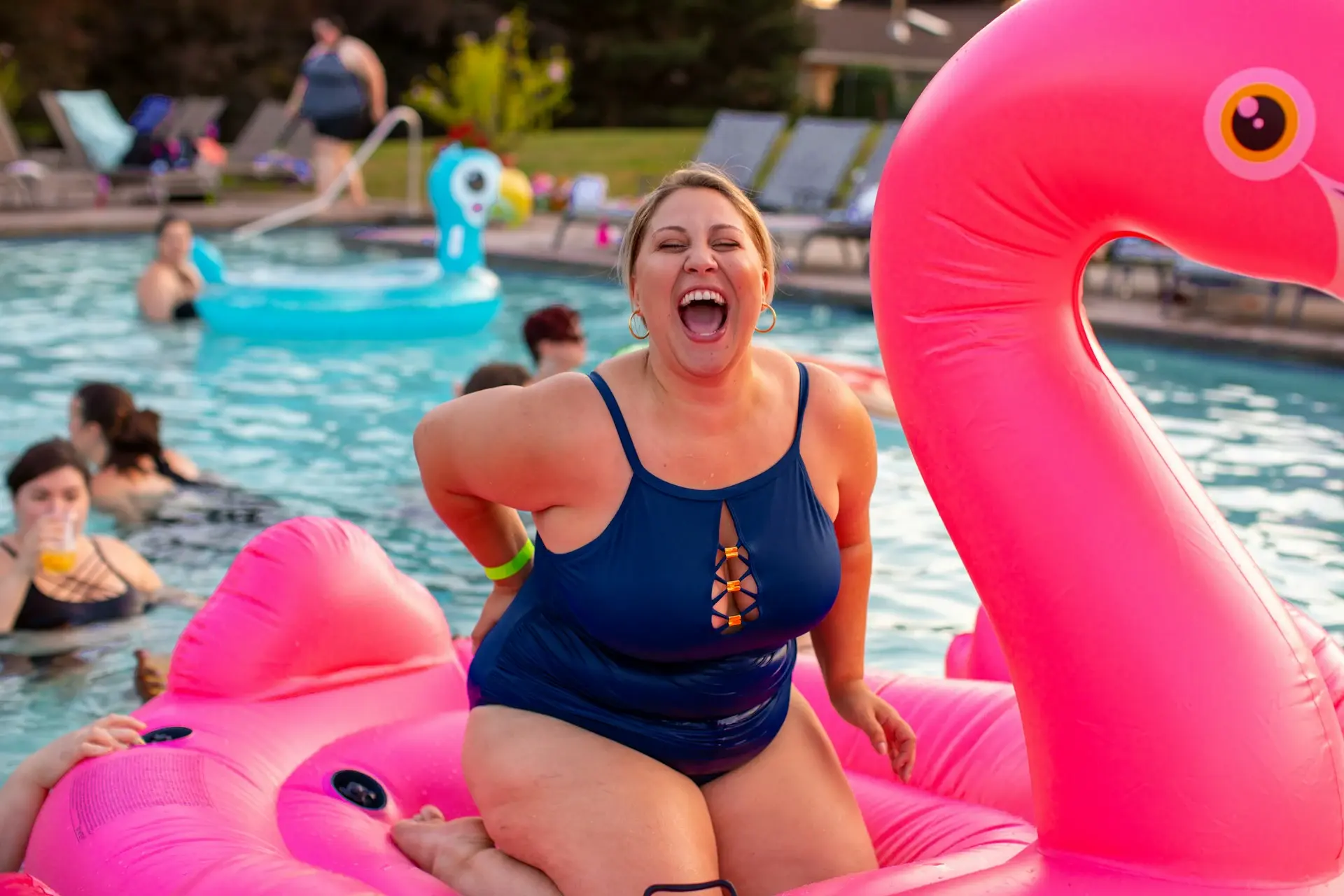 A girl in a swimsuit laughs on a water circle in the form of a flamingo