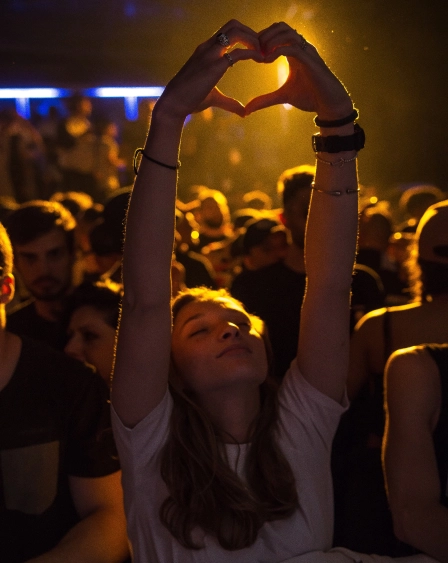 a woman during concert inside a crowd holding her hands high in a shape of a heart
