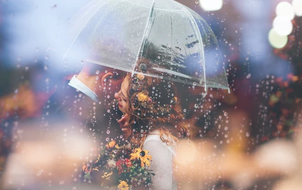 ein Foto von zwei Menschen, die im Regen unter einem Regenschirm kuscheln