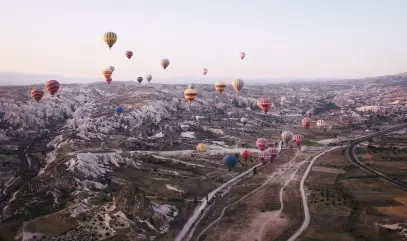 A photo of flying balloons in significant amount in the background of hills covered with sand.
