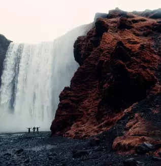 Una foto di una cascata con rocce e anche tre persone ai piedi delle rocce