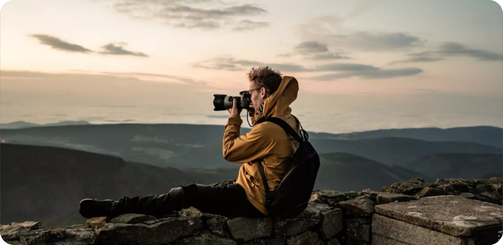 un uomo si siede su una montagna e scatta foto