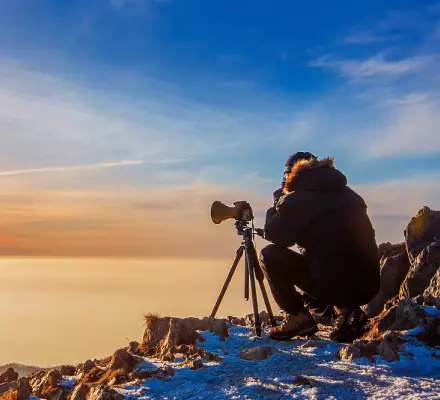 Ein Mann sitzt mit einer Kamera auf einem Berg