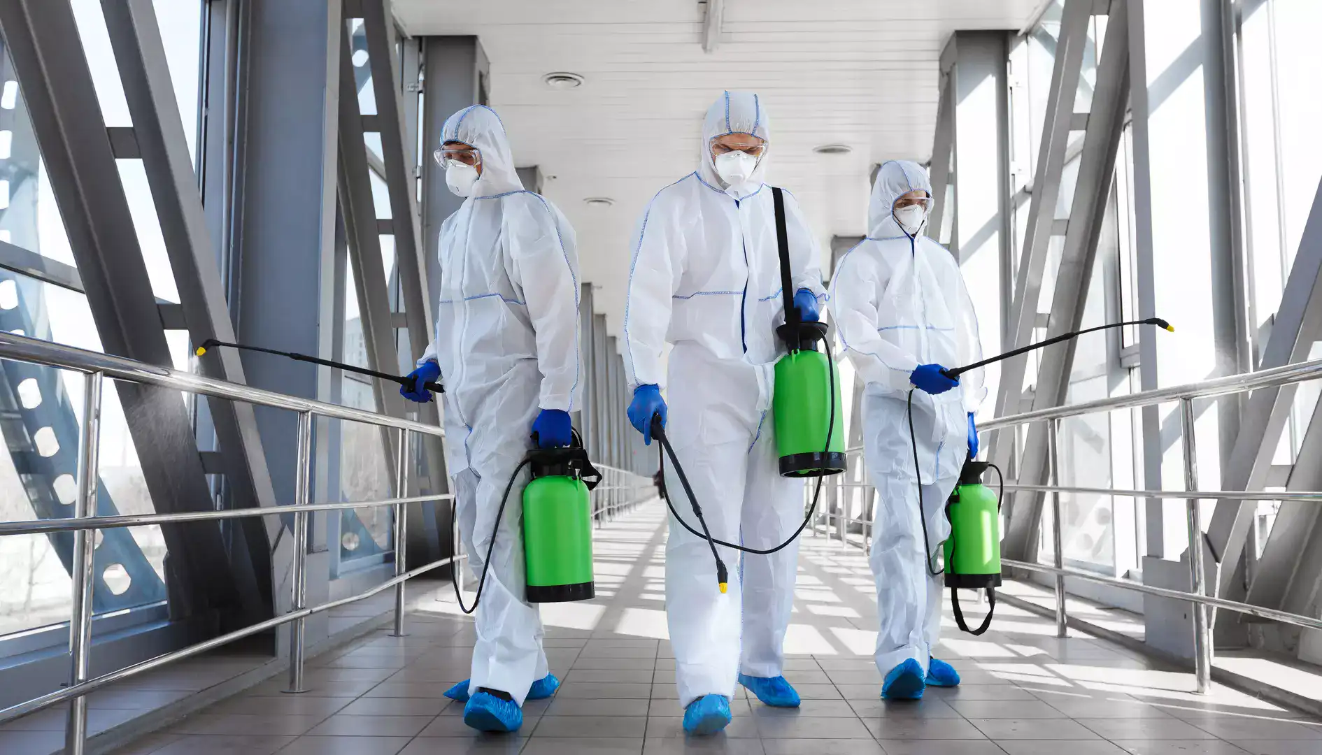 three workers in protective suits carry out disinfection