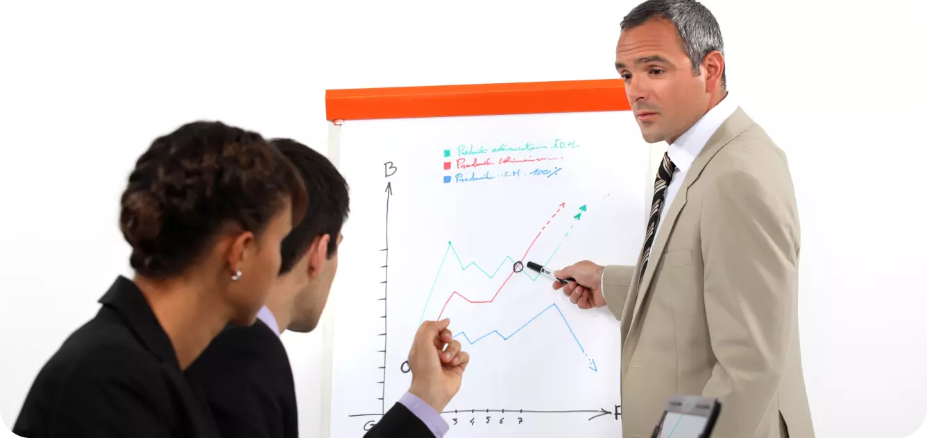 a gray-haired man in a sand jacket presents a graph to two colleagues