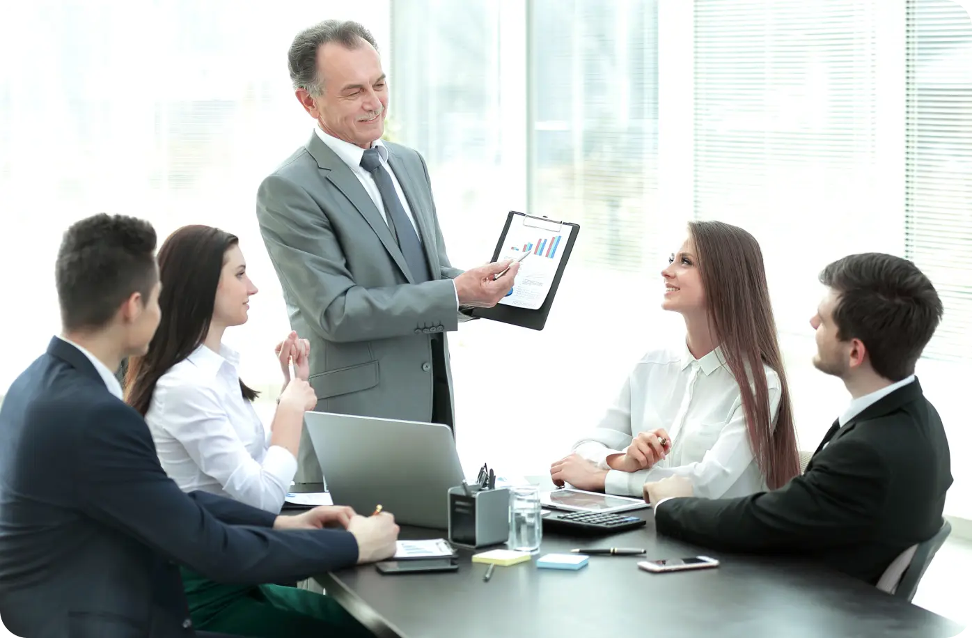 a man in a black suit presents graphs to colleagues