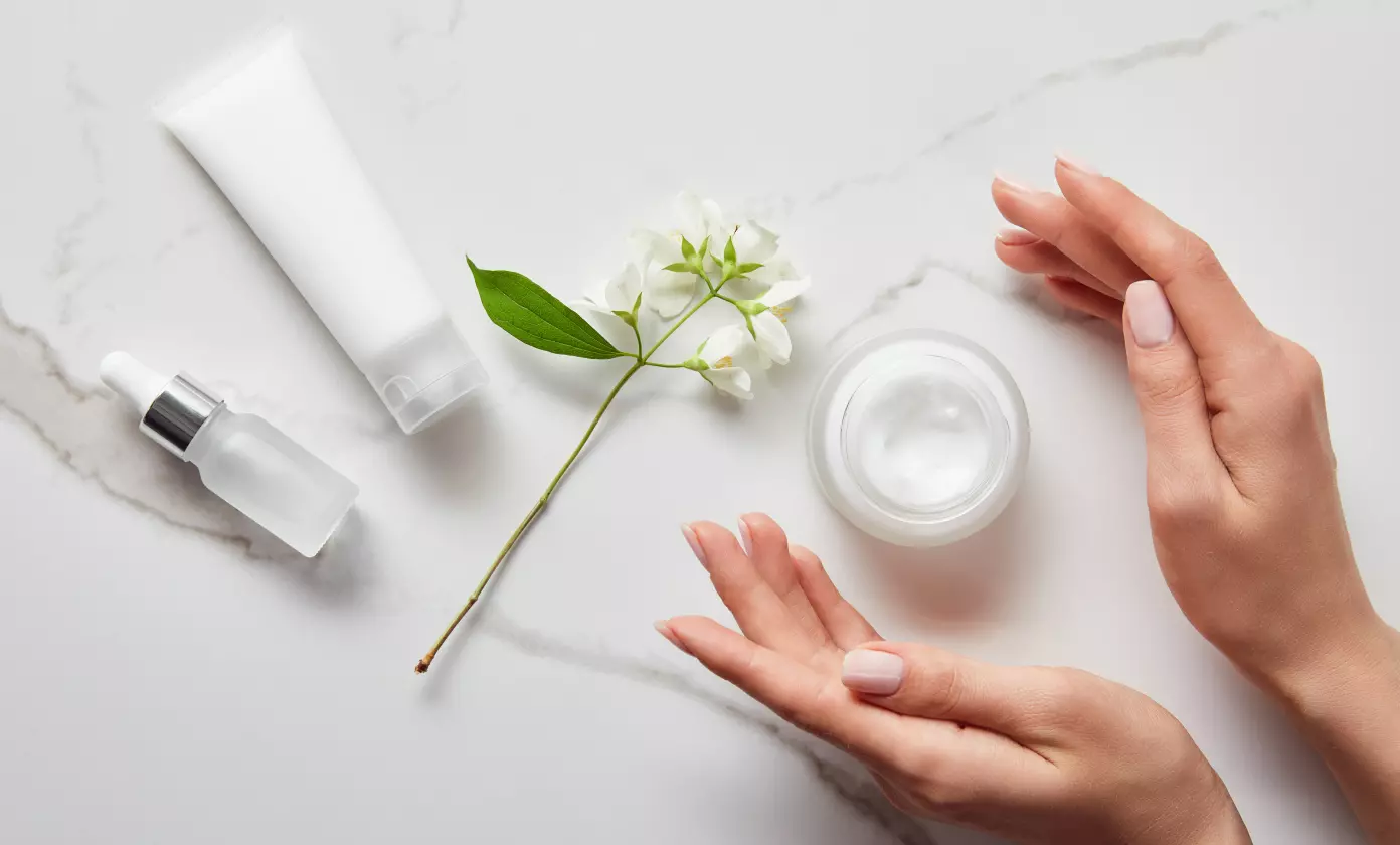 female hands demonstrate hand cream, a sprig of flowers lies nearby