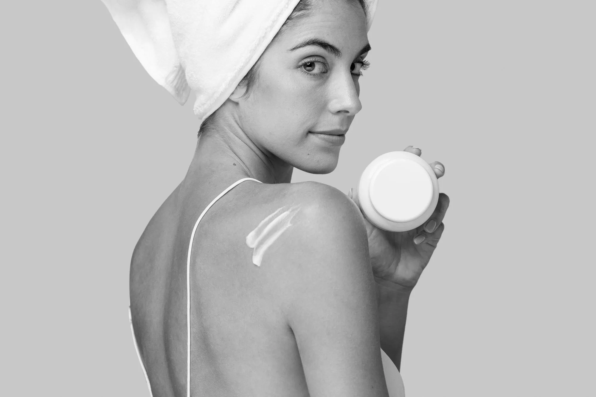 girl in a nightgown applies cream to her body while sitting on the bed