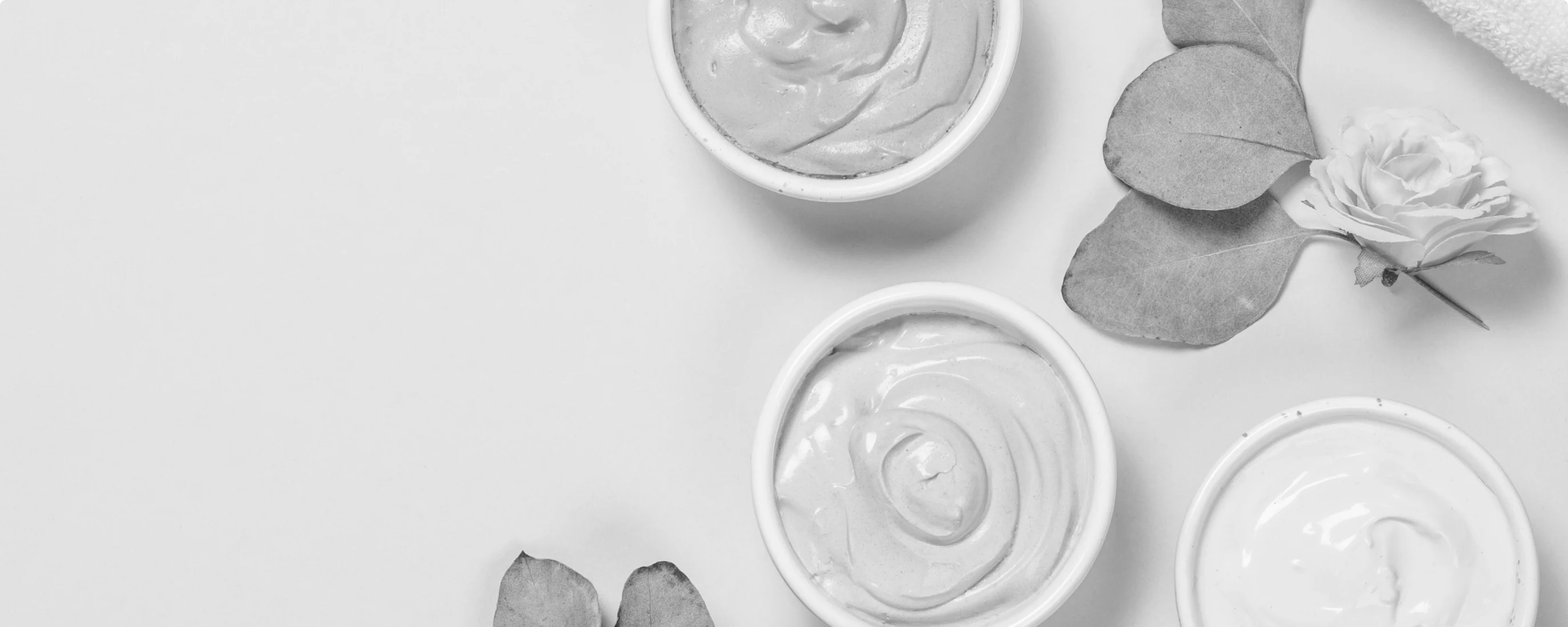 black and white photo of creams and plant leaves on the table, top view