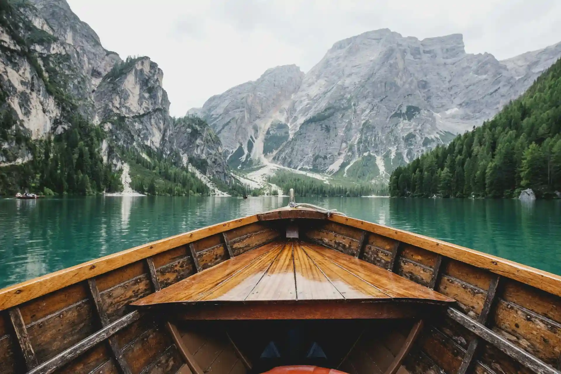 Laivas ant ežero su žaliu vandeniu kalnų fone