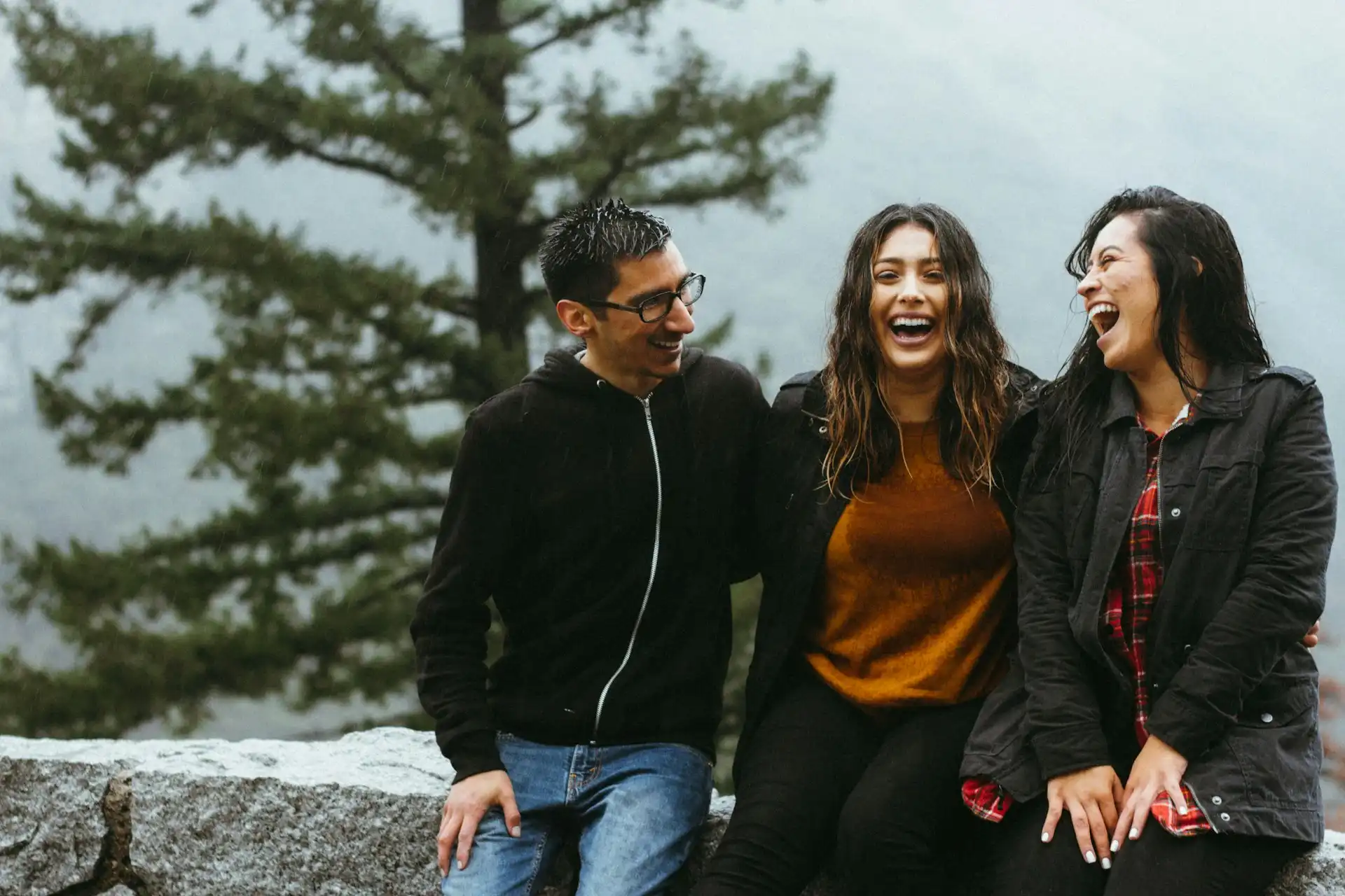 Vaikinas su dviem merginomis stovi kalnuose ir visi plačiai šypsosi