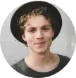 guy with curly blond hair in a black hat