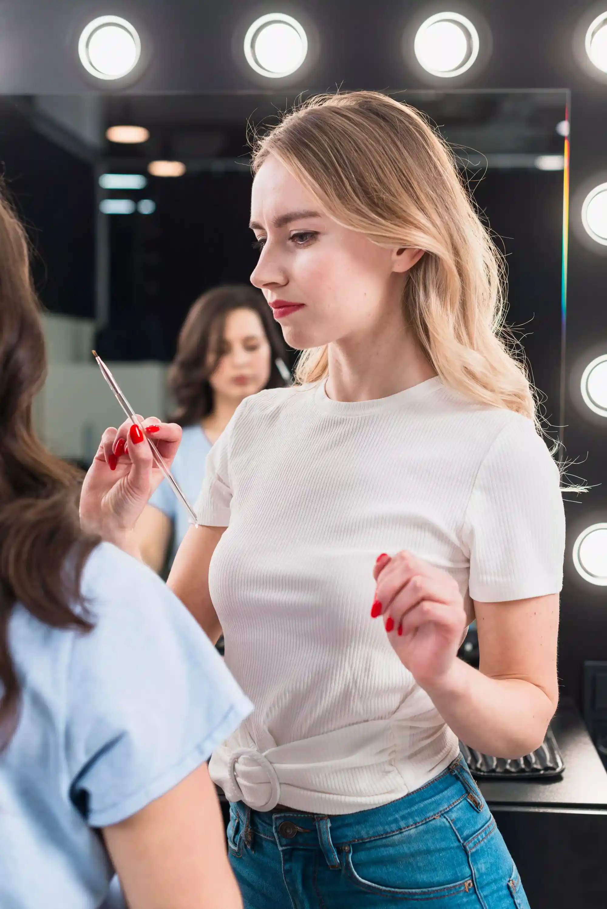 blonde girl with bright red lips applying makeup to another girl