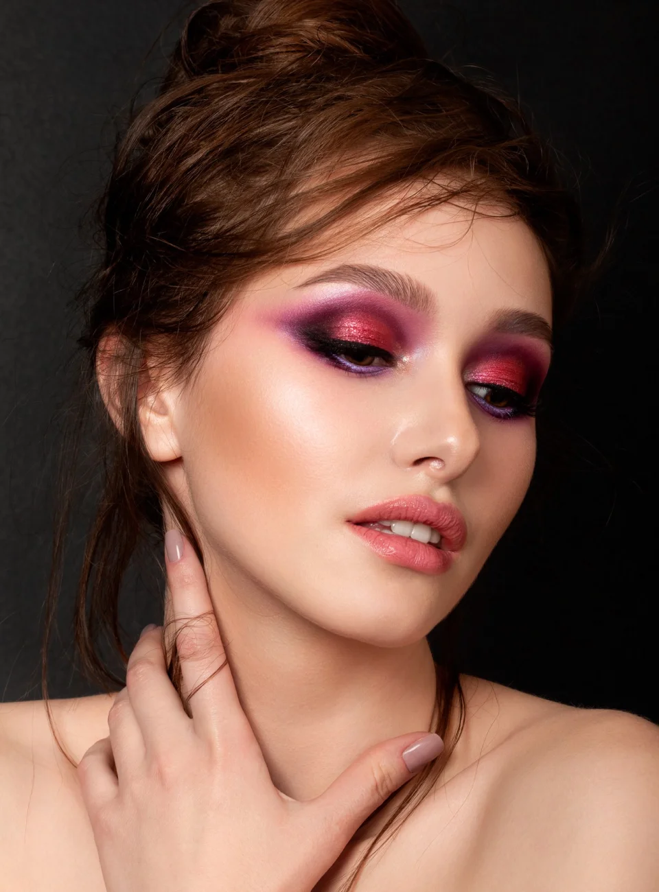 beautiful brown-haired woman with bright pink eye shadow, holds her hands at her neck