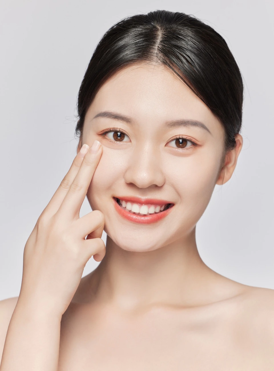 girl with collected hair smiles widely and holds two fingers to her cheek