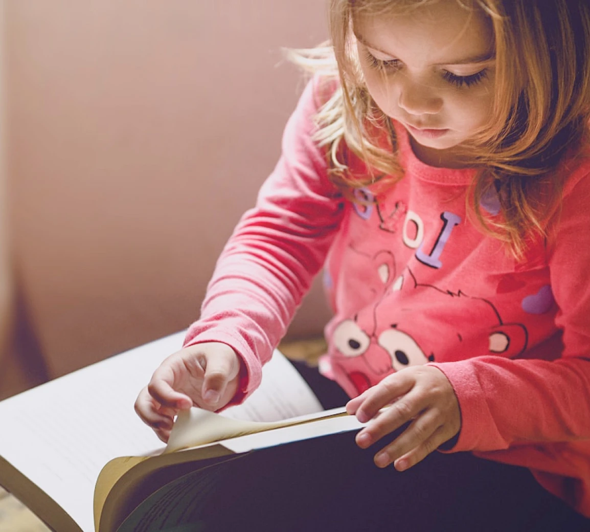 little girl in a pink jacket leafing through a book