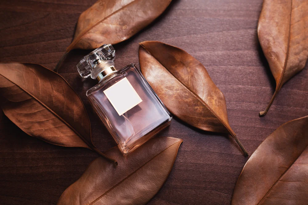 transparent bottle with perfume on a brown table with brown dry leaves of plants