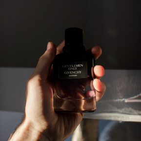 a man's hand holds a bottle with a gradient from black to transparent in the rays of the sun