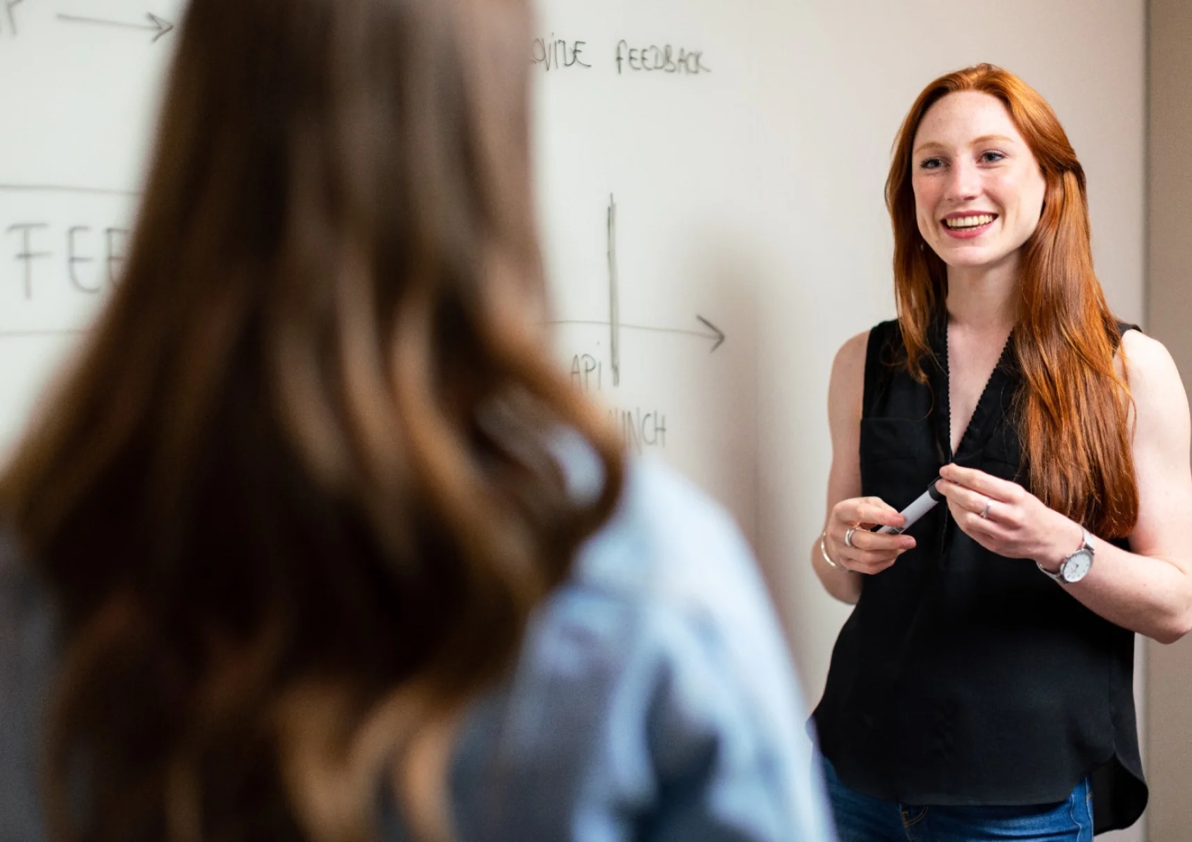red-haired girl teacher smiles at student standing in front of blackboard
