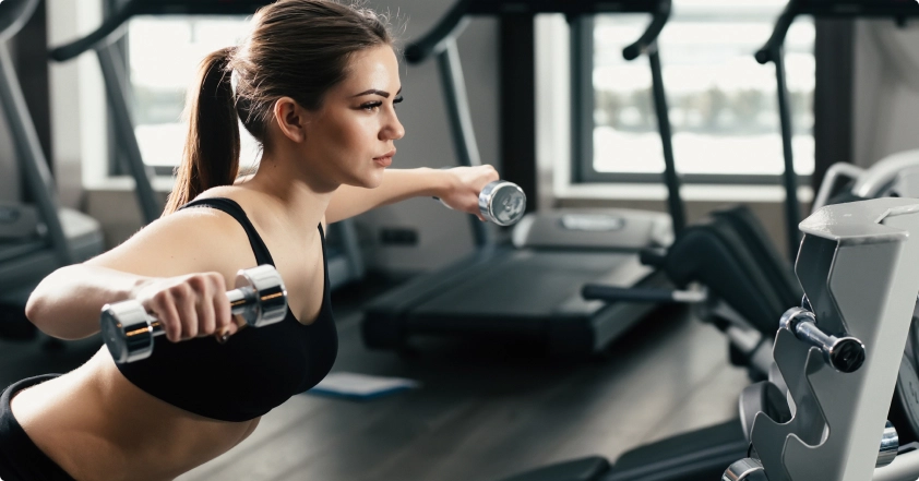 a girl with dark long hair gathered in a ponytail and wearing a black katsuma is working out with dumbbells