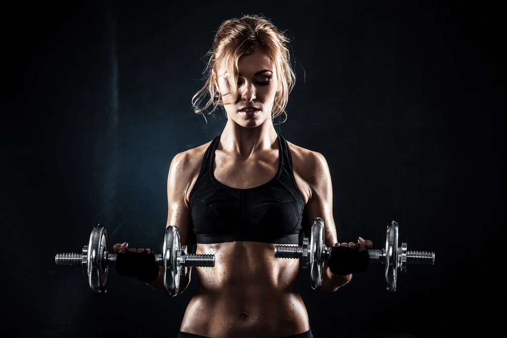 girl with dumbbells in a dark room in the rays of light