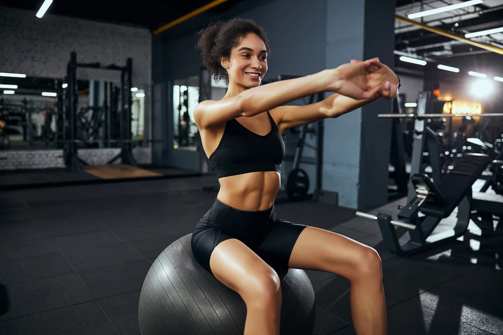 girl smiles and stretches her arms while sitting on a fitball