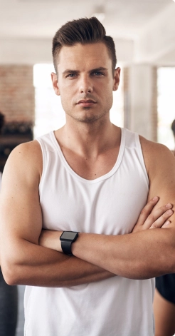 a blond man with a stern look in a white T-shirt stands with folded hands