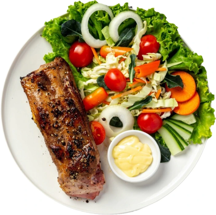 A large piece of meat lies on a plate next to fresh vegetables