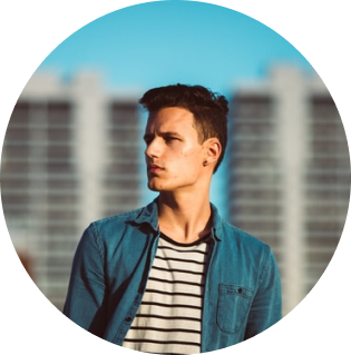 a young guy in a denim shirt and a striped T-shirt looks into the distance against the backdrop of high-rise buildings