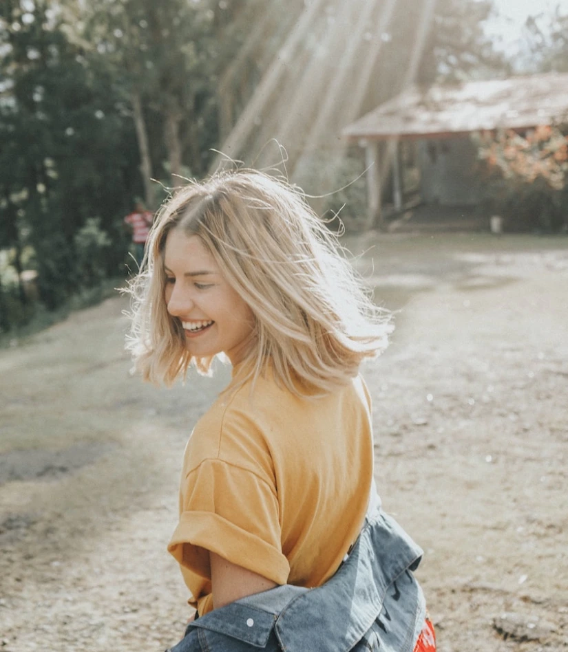 a girl in a yellow T-shirt and denim jacket turns her back and smiles in the sun