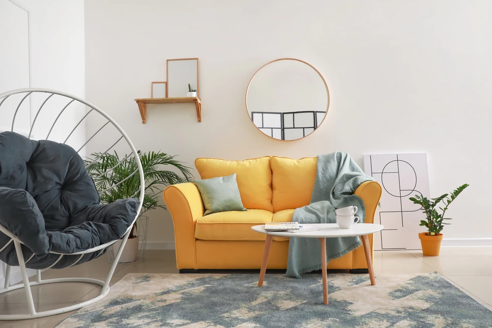 guest room with yellow sofa and gray round chair, as well as gilded furniture and plants