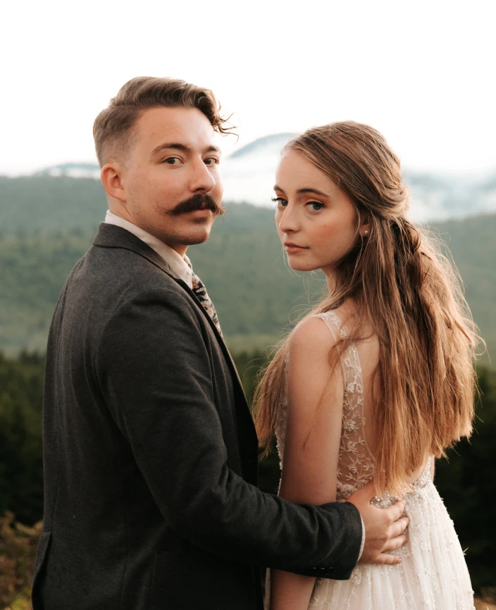 the bride and groom are standing near the mountains