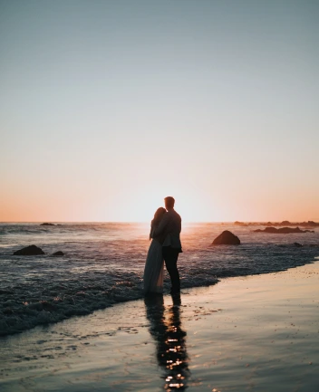 the bride and groom stand by the water