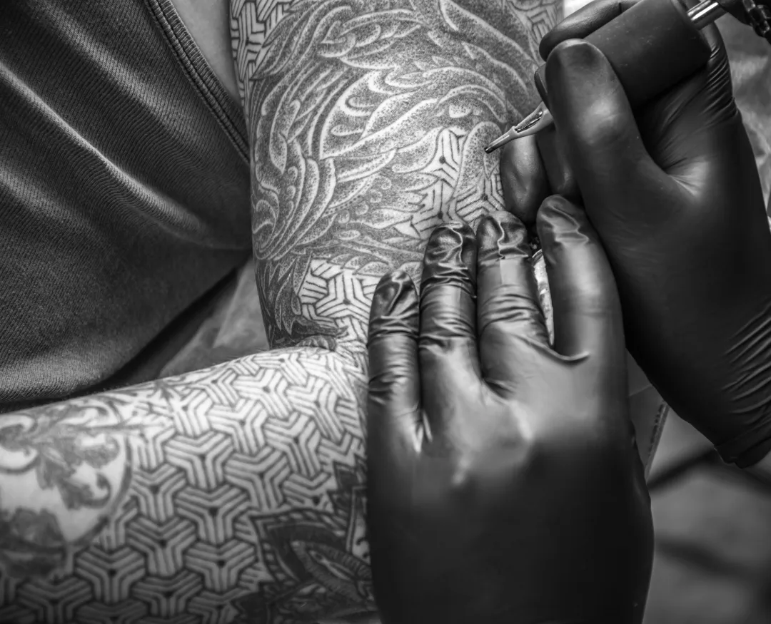 ein Tätowierer füllt ein Tattoo auf dem Arm aus