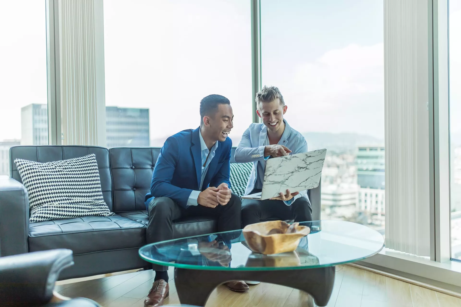 two guys in suits sitting in the office looking at a laptop