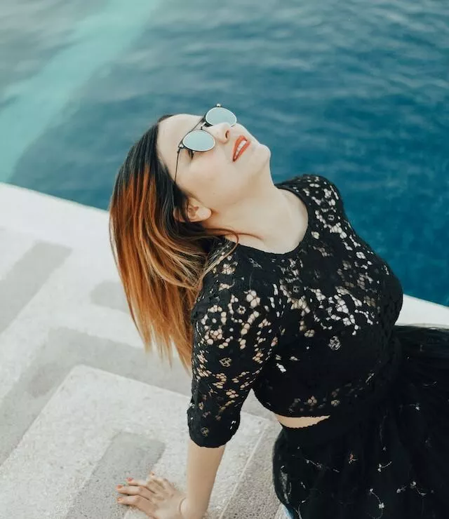 A girl with dark hair in black clothes and sunglasses chides by the pool looking at the sky