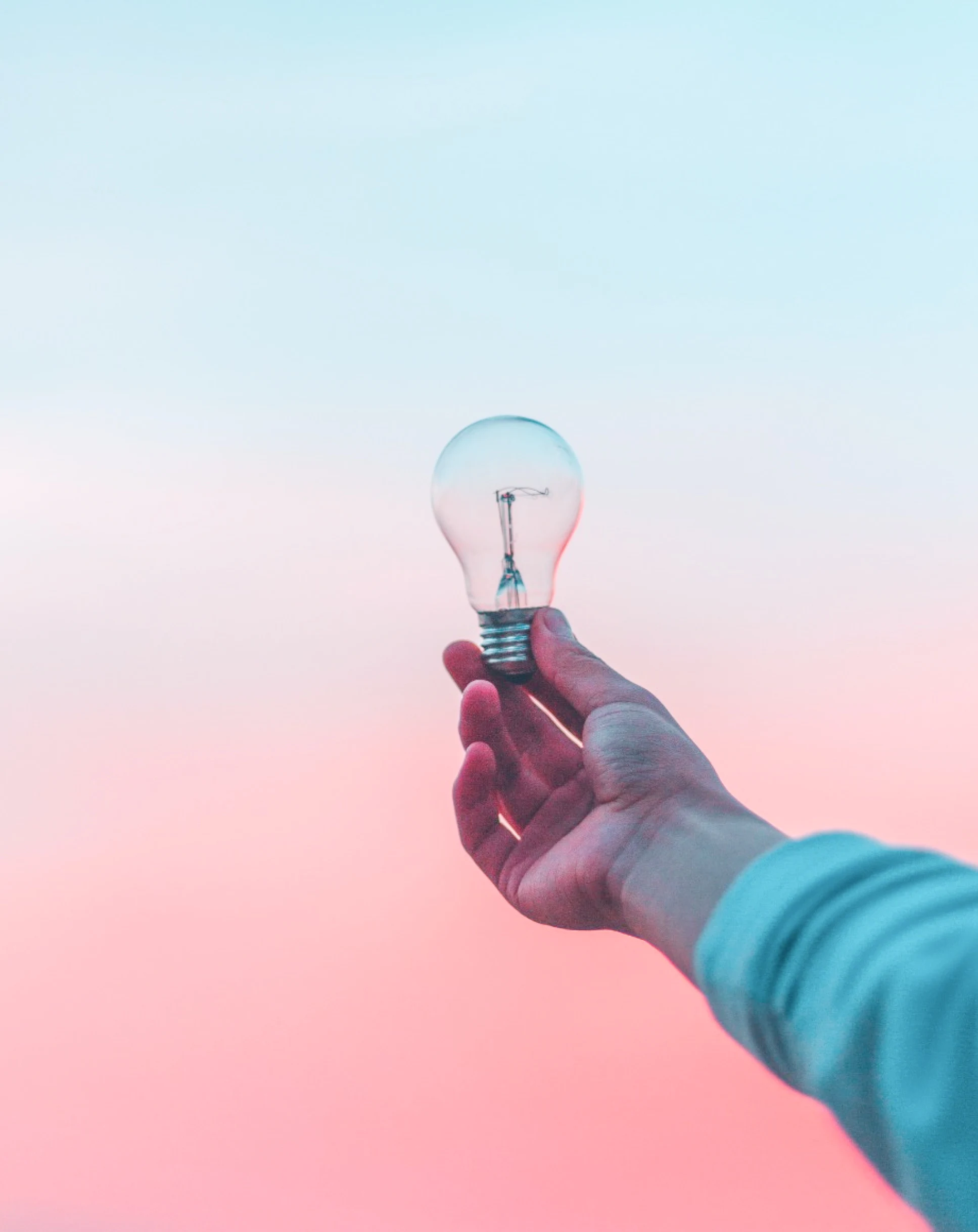 hand holding a light bulb against a background of pink and blue sky