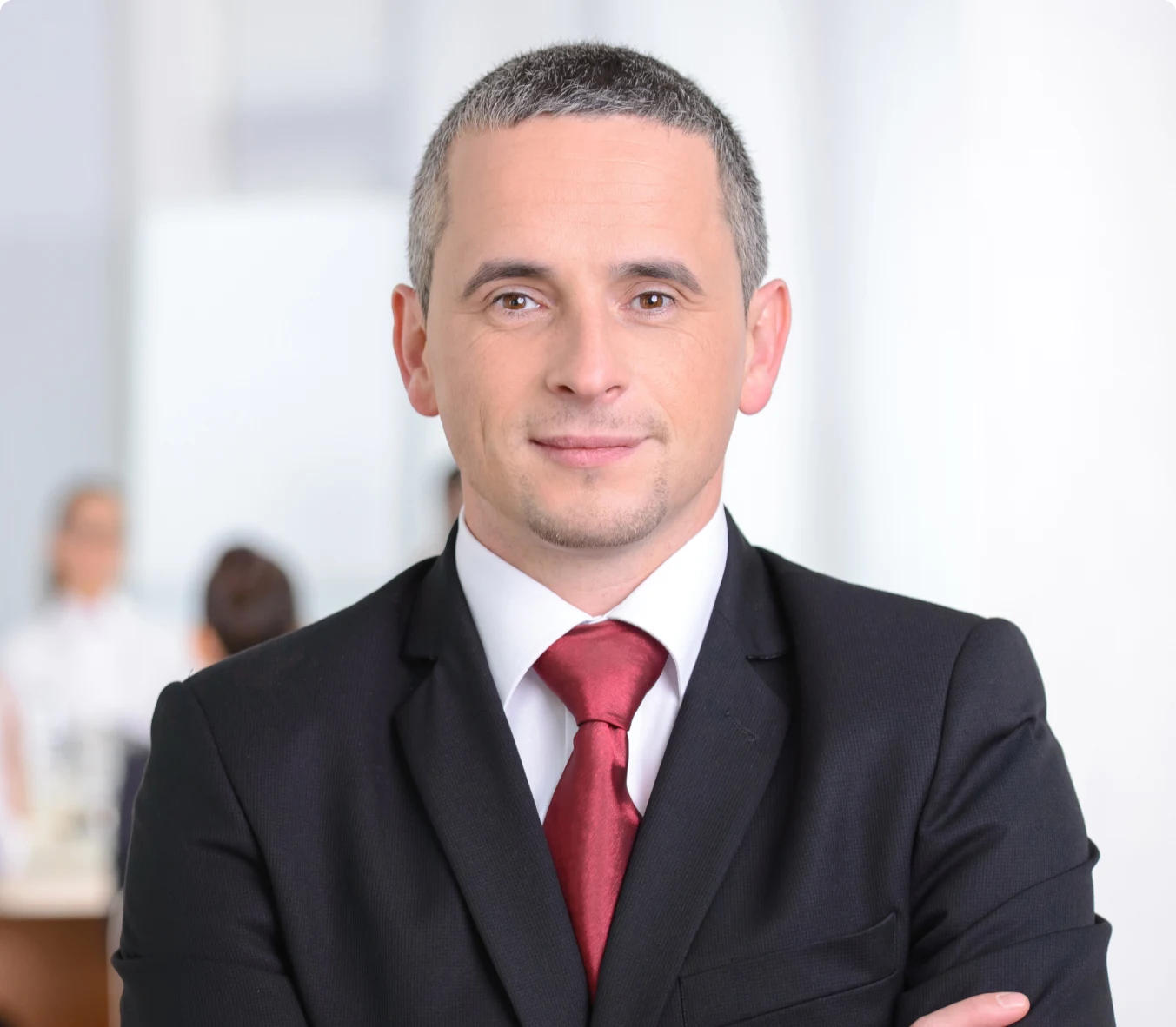 a man with a short haircut, wearing a black suit and a red tie