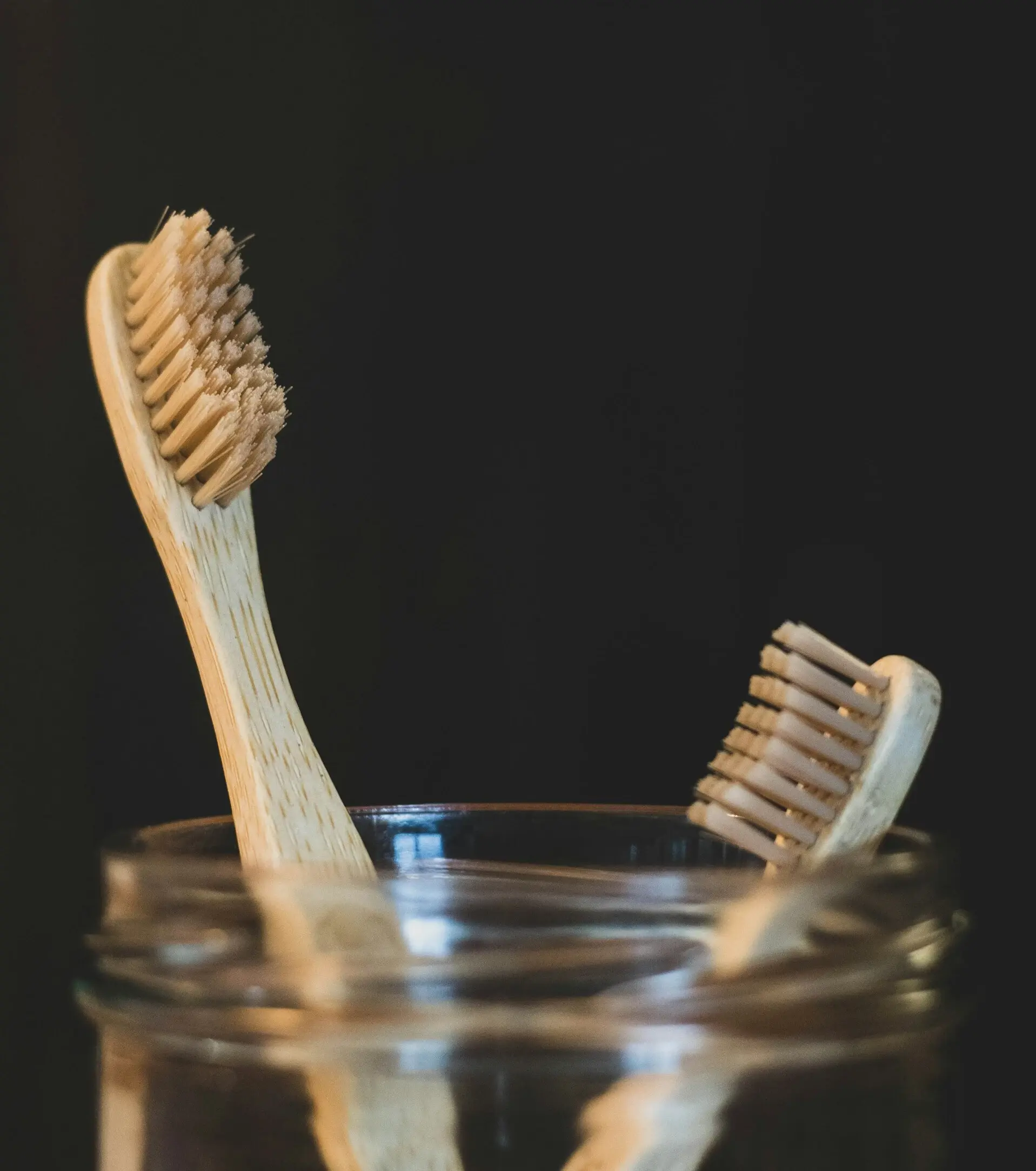 two wooden toothbrushes in a glass jar