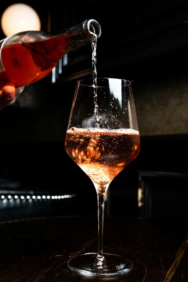Pink champagne is poured from a bottle into a large glass