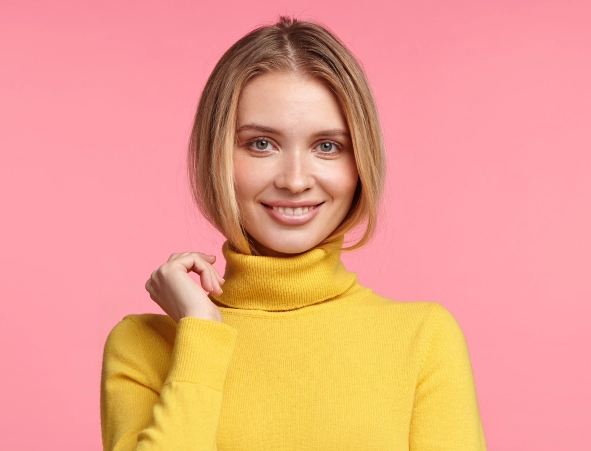 A young blonde girl in a yellow sweater smiles sweetly