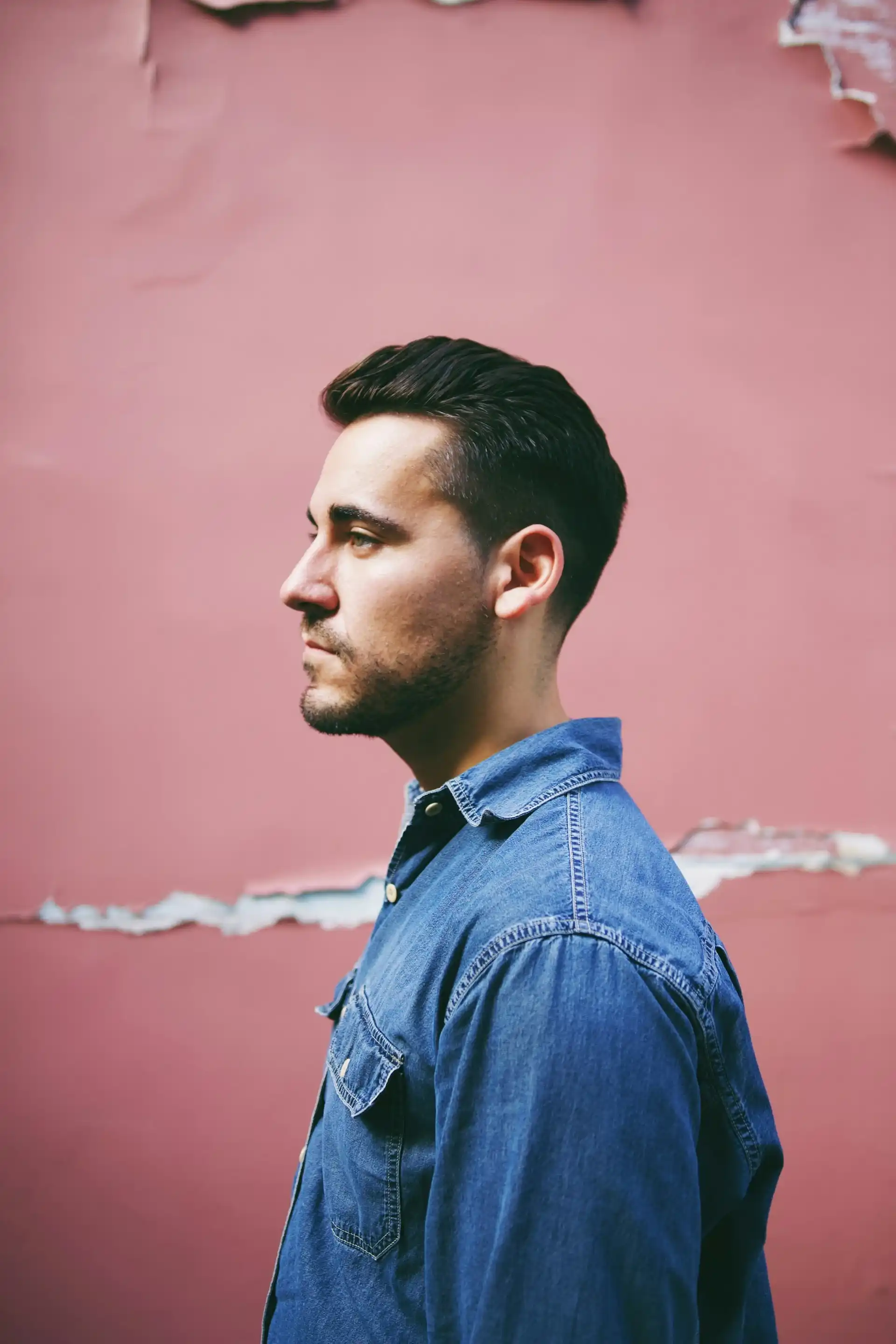 A young guy with dark hair and a denim jacket stands sideways