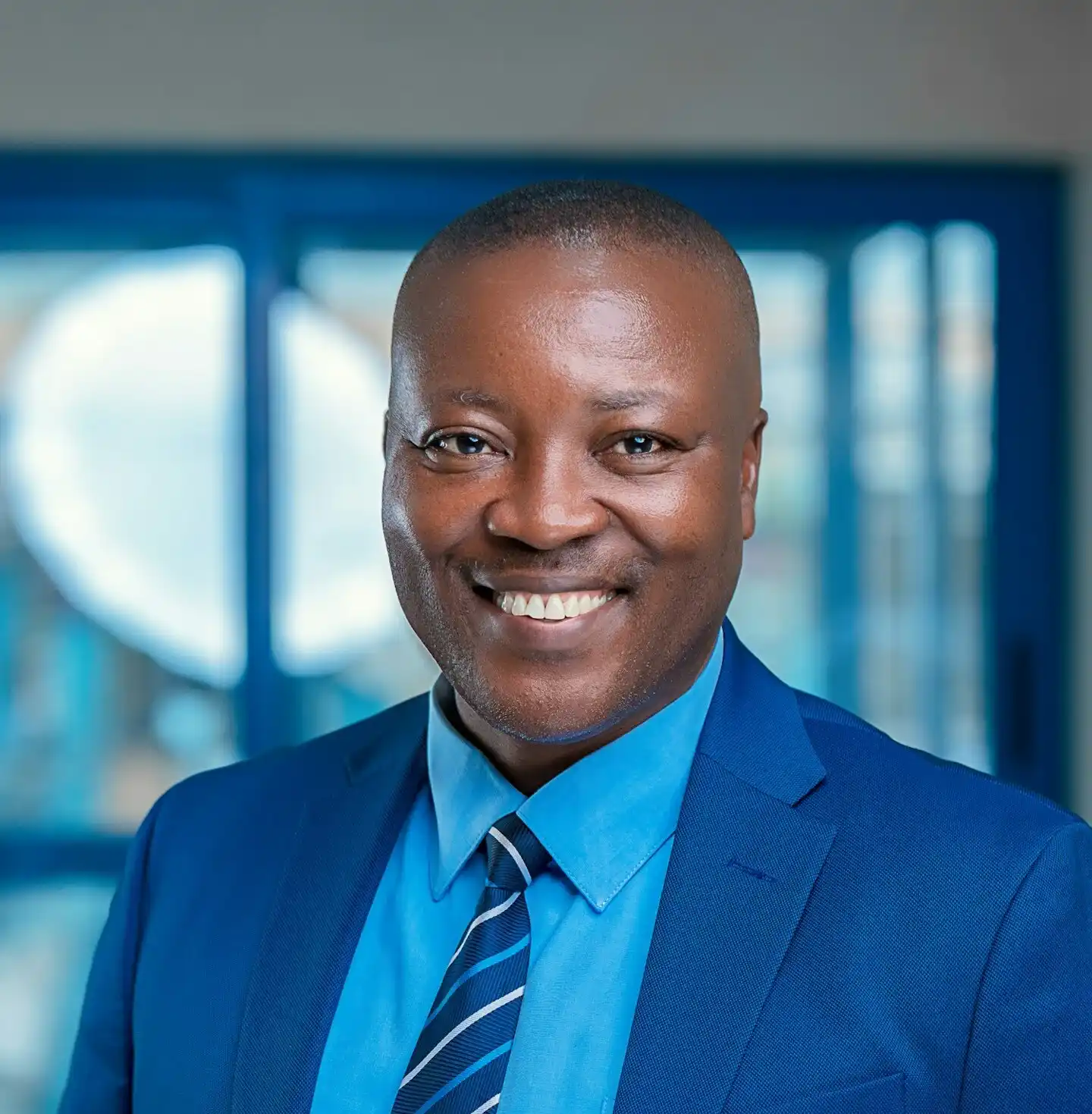 A bald middle-aged man in a formal blue suit smiles widely