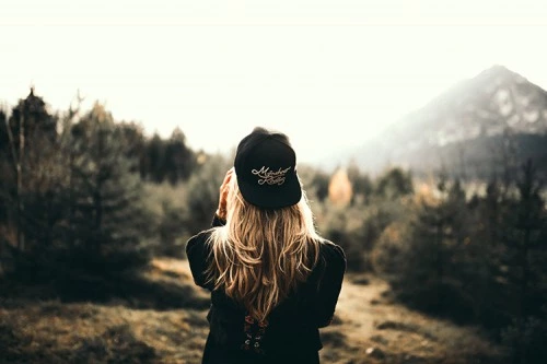 a girl stands near the mountains and next to a tree